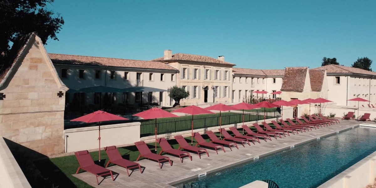 Le couloir de nage et ses transats rouges devant la façade en pierre du Château Fage La Maison des Vignes à Arveyres